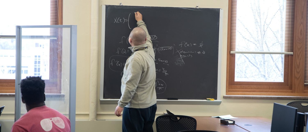 A student writing equations on a blackboard in the Math Tutorial Lab in MacLean Hall