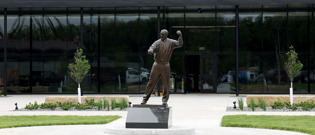 Picture of the outside of the new wrestling training factuality. You see all of the glass windows and a statue of Dan Gable. 