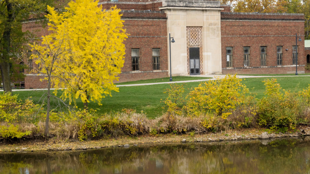 Brick academic building surrounded by trees and water